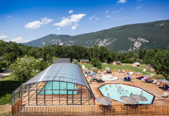 Vakantiepark Huttopia Lac d’Aiguebelette in Auvergne-Rhône-Alpes met zwembad, houten terras en berglandschap.