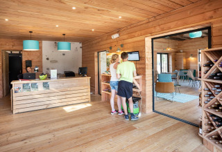 Reception al Huttopia Lac d’Aiguebelette con ospiti, arredo in legno e portabottiglie in Francia.