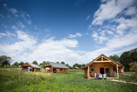 Houten chalets op een grasveld onder een blauwe hemel in Huttopia Lac d’Aiguebelette vakantiepark, Frankrijk.