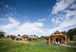 Chalets en bois sur une prairie sous un ciel bleu au parc de vacances Huttopia Lac d’Aiguebelette, France.