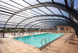 Covered swimming pool with wooden deck and loungers at Huttopia Lac d’Aiguebelette, Auvergne-Rhône-Alpes, France.