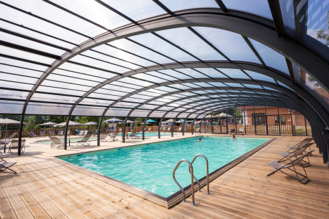 Überdachtes Schwimmbad mit Holzdeck und Liegen im Huttopia Lac d’Aiguebelette, Auvergne-Rhône-Alpes, Frankreich.