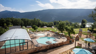 Vista de la zona de la piscina y el parque infantil en Huttopia Lac d’Aiguebelette en Auvernia-Ródano-Alpes, Francia.