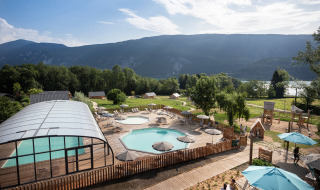 Vista de la zona de la piscina y el parque infantil en Huttopia Lac d’Aiguebelette en Auvernia-Ródano-Alpes, Francia.