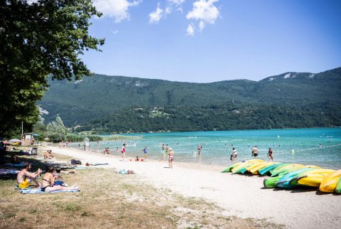 Personas descansando junto al lago turquesa en Huttopia Lac d’Aiguebelette, Auvergne-Rhône-Alpes, Francia.