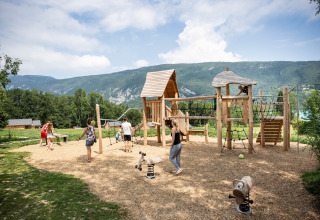 Kinderen en volwassenen spelen op een natuurlijke speeltuin in Huttopia Lac d’Aiguebelette met bergen rondom.