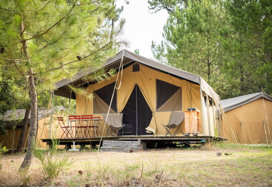 Tente safari Toile&Bois tent Sweet en forêt, terrasse aménagée, chaises rouges, entourée d’arbres.