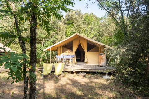 Tienda safari Bungalow tent Classic entre árboles, con terraza, sillas y mesa al aire libre en el bosque.
