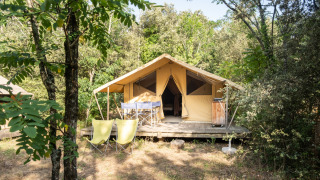 Bungalow tent Classic safari telt omgivet af træer, med terrasse, stole og bord i en naturskøn skov.