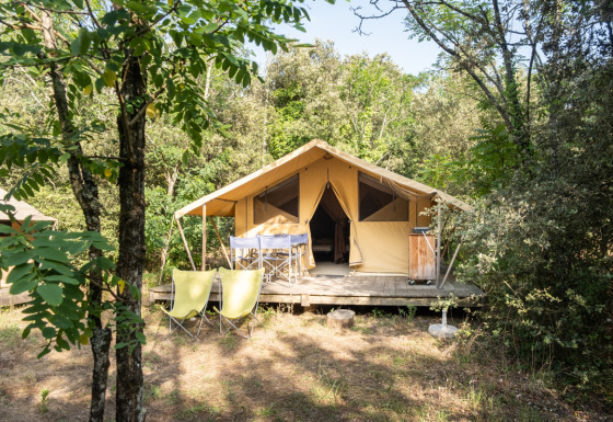 Tienda safari Bungalow tent Classic entre árboles, con terraza, sillas y mesa al aire libre en el bosque.