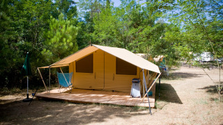 Tienda safari llamada Toile&bois Tent Classic con plataforma de madera en un camping verde y frondoso.