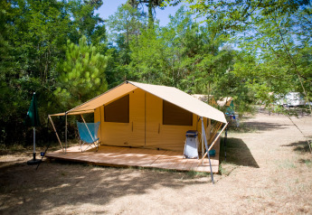 Tenda safari chiamata Toile&bois Tent Classic con terrazza in legno in un campeggio verdeggiante nel bosco.