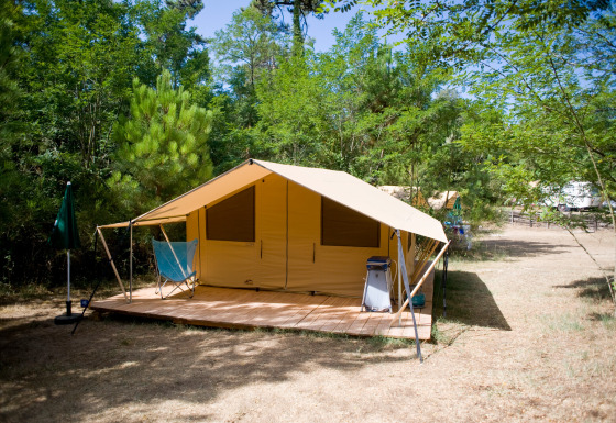 Tente safari appelée Toile&bois Tent Classic sur terrasse en bois, installée dans un camping forestier verdoyant.