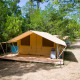 Tienda safari llamada Toile&bois Tent Classic con plataforma de madera en un camping verde y frondoso.