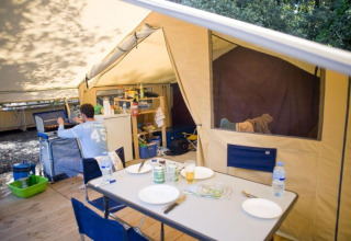 Vista interna di una tenda safari con tavolo, cucina e una persona a Huttopia Oléron les Pins, Francia.