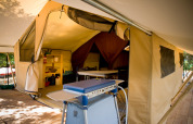 Interno di una tenda safari Toile&bois Classic a Huttopia Oléron les Pins, Francia, con cucina e tavolo.