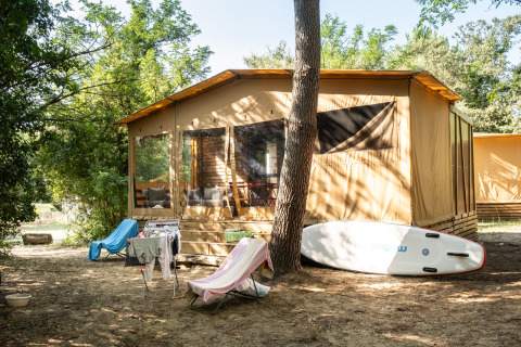 Arizona-safaritent in een bosrijke omgeving met ligstoelen, droogrekje en stand up paddle board.