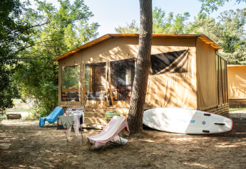 Tienda safari Arizona en un entorno boscoso, con sillas plegables, tendedero y tabla de paddle surf.