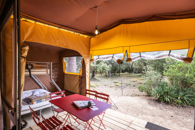 Interior de tienda safari Arizona en Huttopia Oléron les Pins con literas, mesa roja y vistas al bosque.