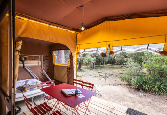 Interior de tienda safari Arizona en Huttopia Oléron les Pins con literas, mesa roja y vistas al bosque.