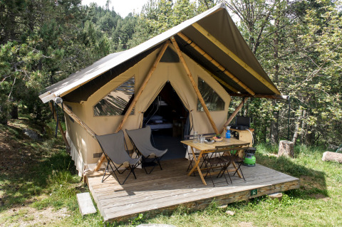 Safari-Zeltkanadianer mit Holzveranda, Campingstühlen und Tisch, umgeben von Bäumen im Wald.