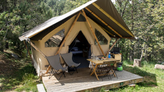 A Canadian safari tent cabin with wooden veranda, camping chairs, and table set in a forested area.