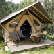 En canadisk safaritelts hytte med træveranda, campingstole og bord midt i en skovklædt natur.