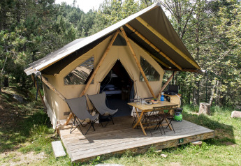 Tente safari canadienne avec véranda en bois, chaises et table, située au cœur d’une zone boisée.