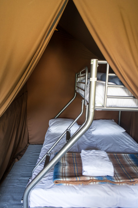 Vista interior de una tienda safari con literas y ropa de cama en Huttopia Font-Romeu, Francia.