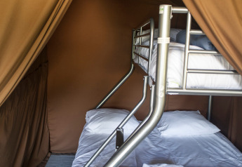 Binnenzicht van een safari tent met stapelbedden en lakens in Huttopia Font-Romeu, Frankrijk.