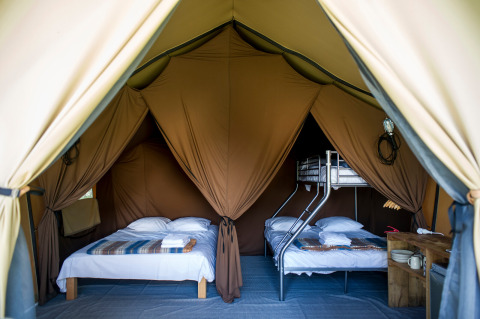Interior de una tienda safari canadiense con cama doble y litera en Huttopia Font-Romeu, Francia.