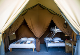 Interieur van een Canadees safaritent met tweepersoonsbed en stapelbed bij Huttopia Font-Romeu, Frankrijk.