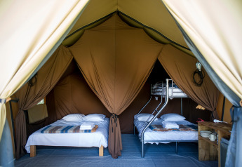 Binnenkant van een Canadese safaritent met tweepersoonsbed en stapelbed bij Huttopia Font-Romeu, Frankrijk.