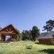 Træhytter omgivet af træer og græs under blå himmel ved Chalet 'The Cabin' i en naturskøn dal.