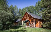 En hyggelig træhytte med terrasse, omgivet af grønne træer ved Huttopia Font-Romeu, Frankrig, på en solskinsdag.