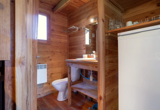 Interieur van chaletbadkamer met houten wanden, toilet, wastafel, spiegel en koelkast in Huttopia Font-Romeu.