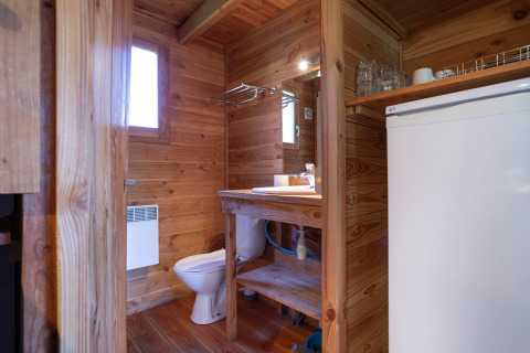 Interno di bagno chalet con rivestimento in legno, wc, lavandino, specchio e frigo a Huttopia Font-Romeu.