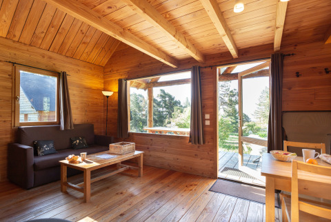 Interior de madera del Chalet 'The Cabin' en Huttopia Font-Romeu, Francia, con vistas al jardín exterior.