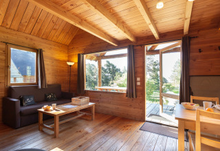 Interior de madera del Chalet 'The Cabin' en Huttopia Font-Romeu, Francia, con vistas al jardín exterior.