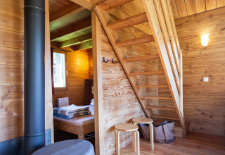 Vista interior de la cabaña Chalet 'The Cabin' con escaleras, estufa y cama en Huttopia Font-Romeu.