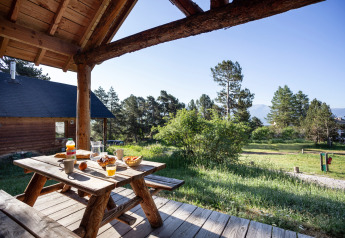 Wooden picnic table set for breakfast on a cabin porch overlooking trees at Huttopia Font-Romeu, France.