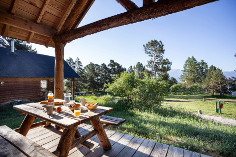 Tavolo da picnic in legno apparecchiato per colazione su veranda, vista natura a Huttopia Font-Romeu, Francia.