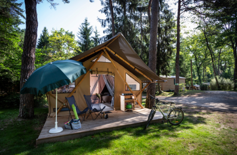Tienda safari Trappeur en Huttopia Font-Romeu, Francia, con terraza, bicicleta y sombrilla en el bosque.