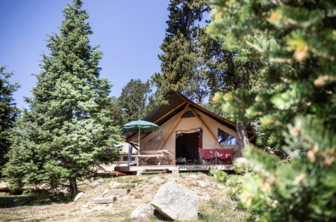Tienda safari Trappeur en Huttopia Font-Romeu, Francia, rodeada de árboles verdes y naturaleza montañosa.