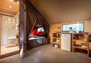 Interior de una tienda safari Trappeur en Huttopia Font-Romeu, Francia, con baño, cocina y cama visibles.
