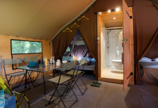 Interior de una lujosa tienda safari Trappeur con comedor, camas y baño en Huttopia Font-Romeu, Francia.