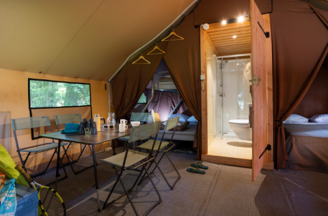 Interior de una lujosa tienda safari Trappeur con comedor, camas y baño en Huttopia Font-Romeu, Francia.