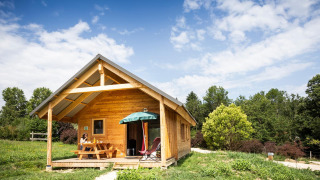 Houten Chalet Montana met veranda, picknicktafel en prachtige natuur onder een heldere blauwe lucht.