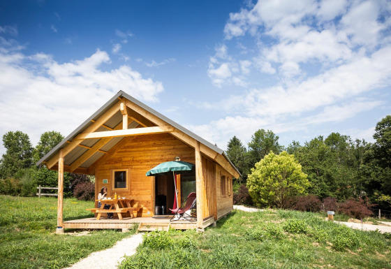 Houten Chalet Montana met overdekt terras, picknicktafel en veel groen onder een blauwe lucht.