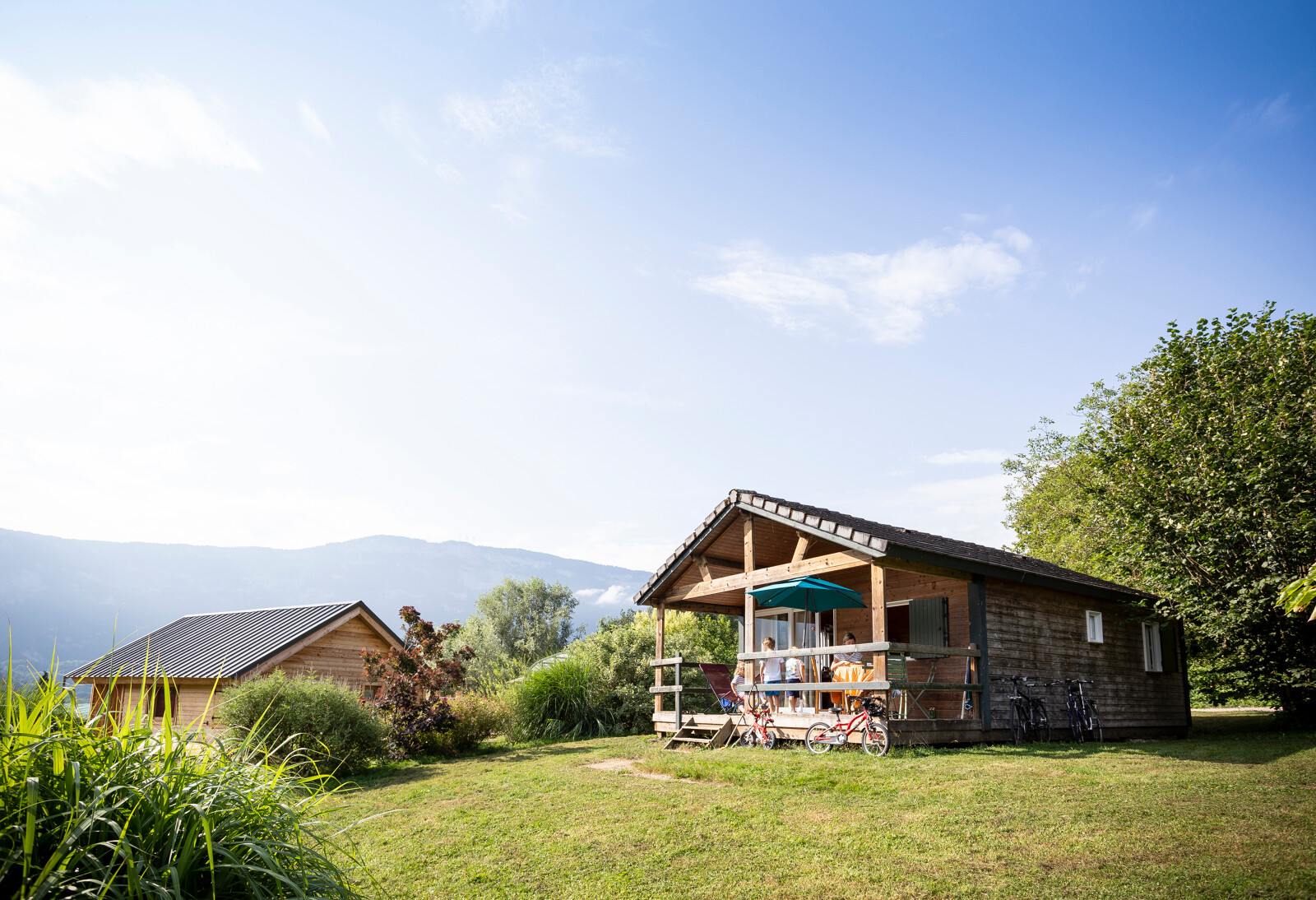 Chalet Montana, een houten hut met veranda en fietsen, omgeven door natuur bij Huttopia Lac d'Aiguebelette, Frankrijk.